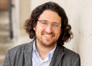 Portrait of Devin Naar, smiling, in suit jacket