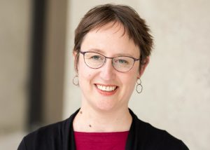 Liora Halperin smiling, wearing glasses, with paired shirt and sweater